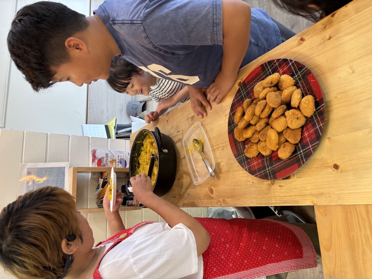 A student receiving a plate of croquettes from the teacher in a red apron