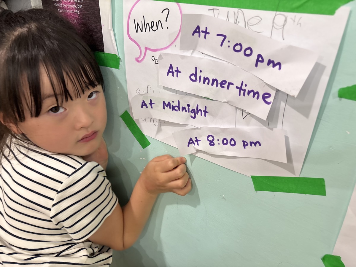 A young student in a striped shirt at the wall beside the When question chart