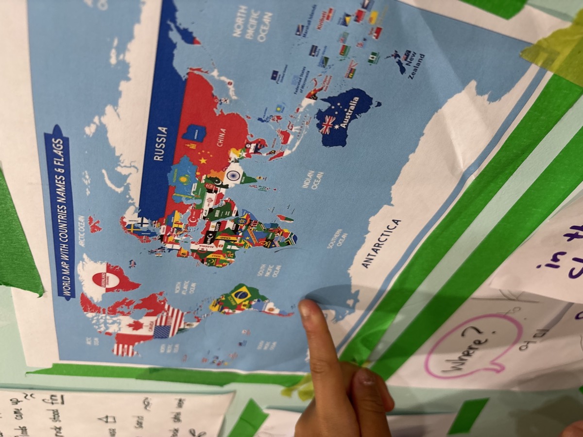 A student pointing at a world map with country flags beside the Where question