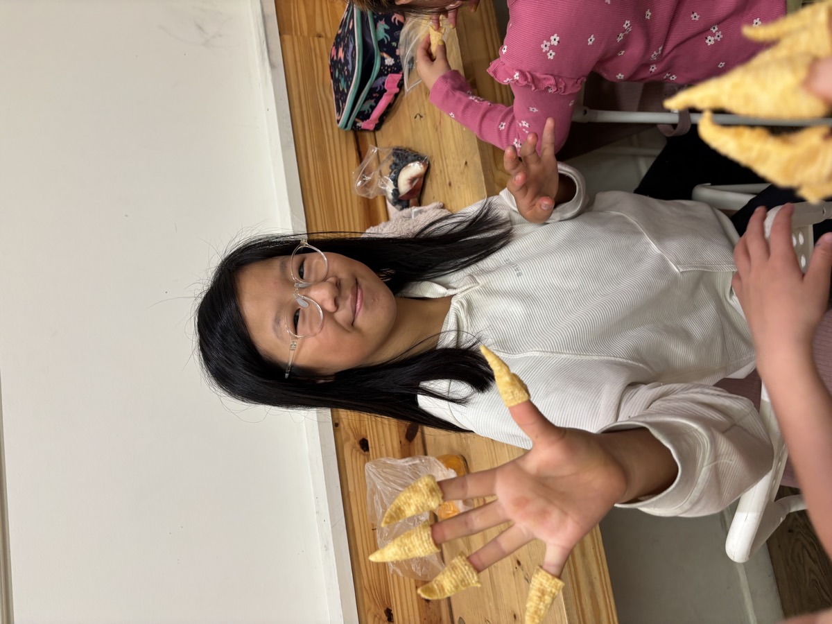 Two students laughing and comparing the corn snacks stuck on their fingertips