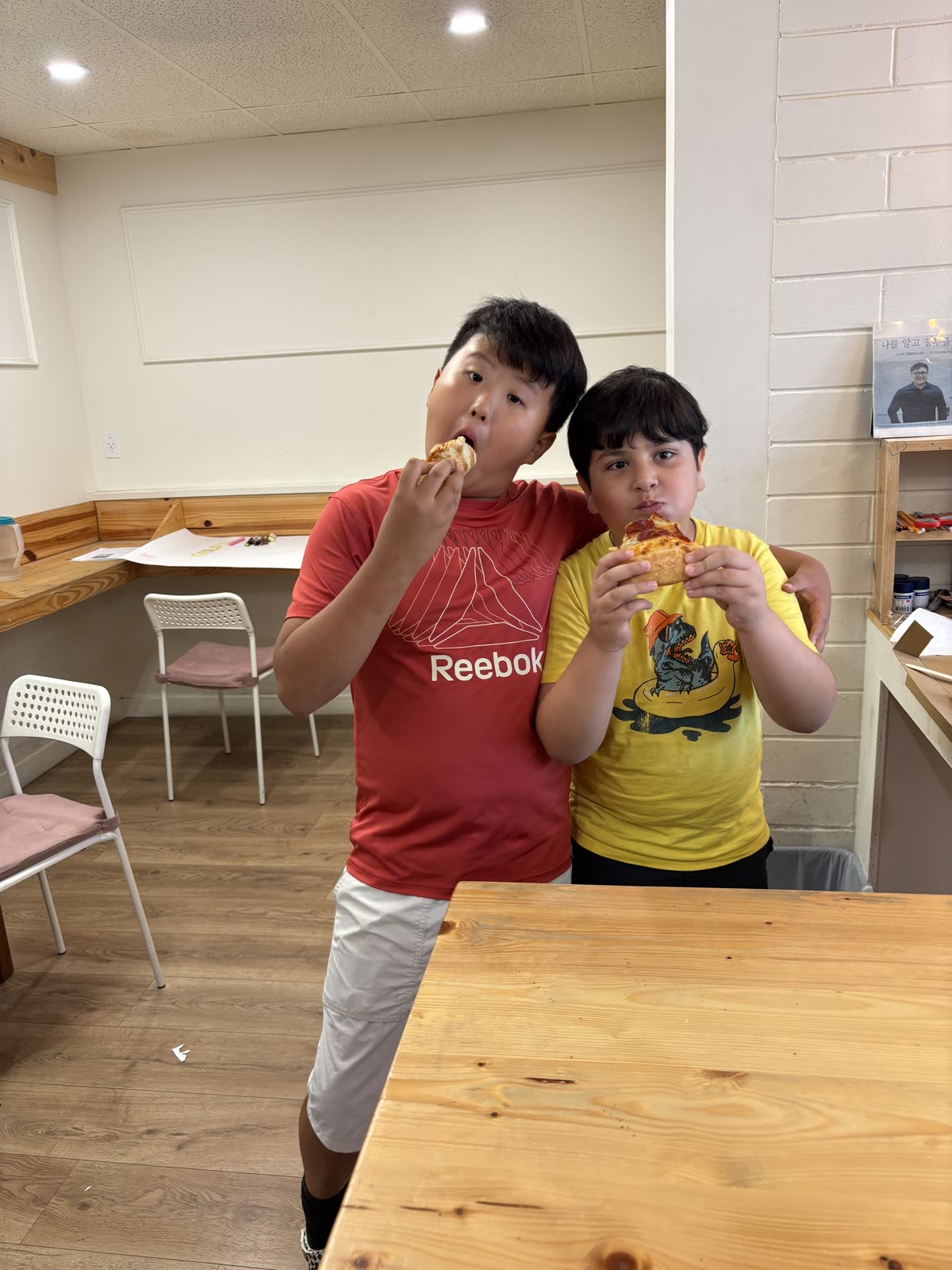Two friends standing together while eating pizza