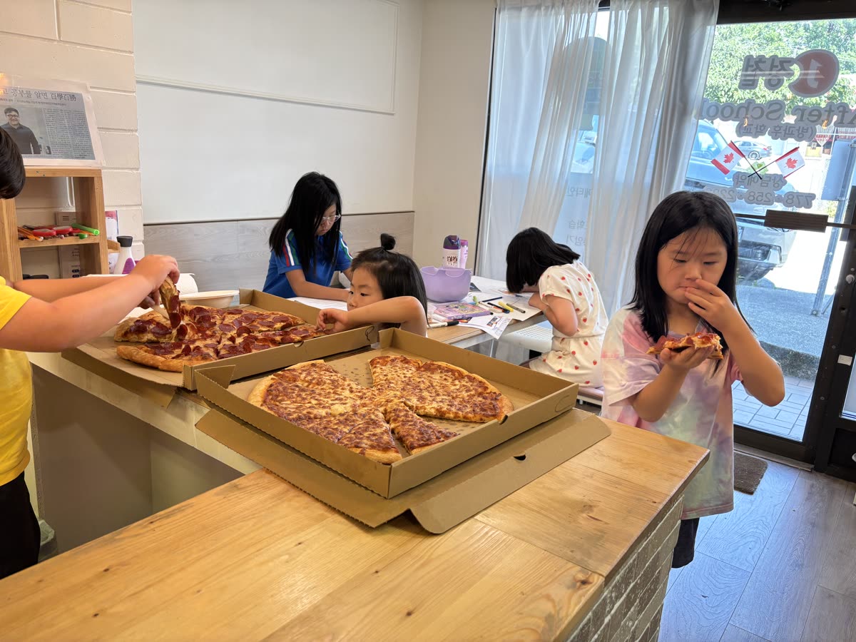 Two open pizza boxes surrounded by students in the classroom