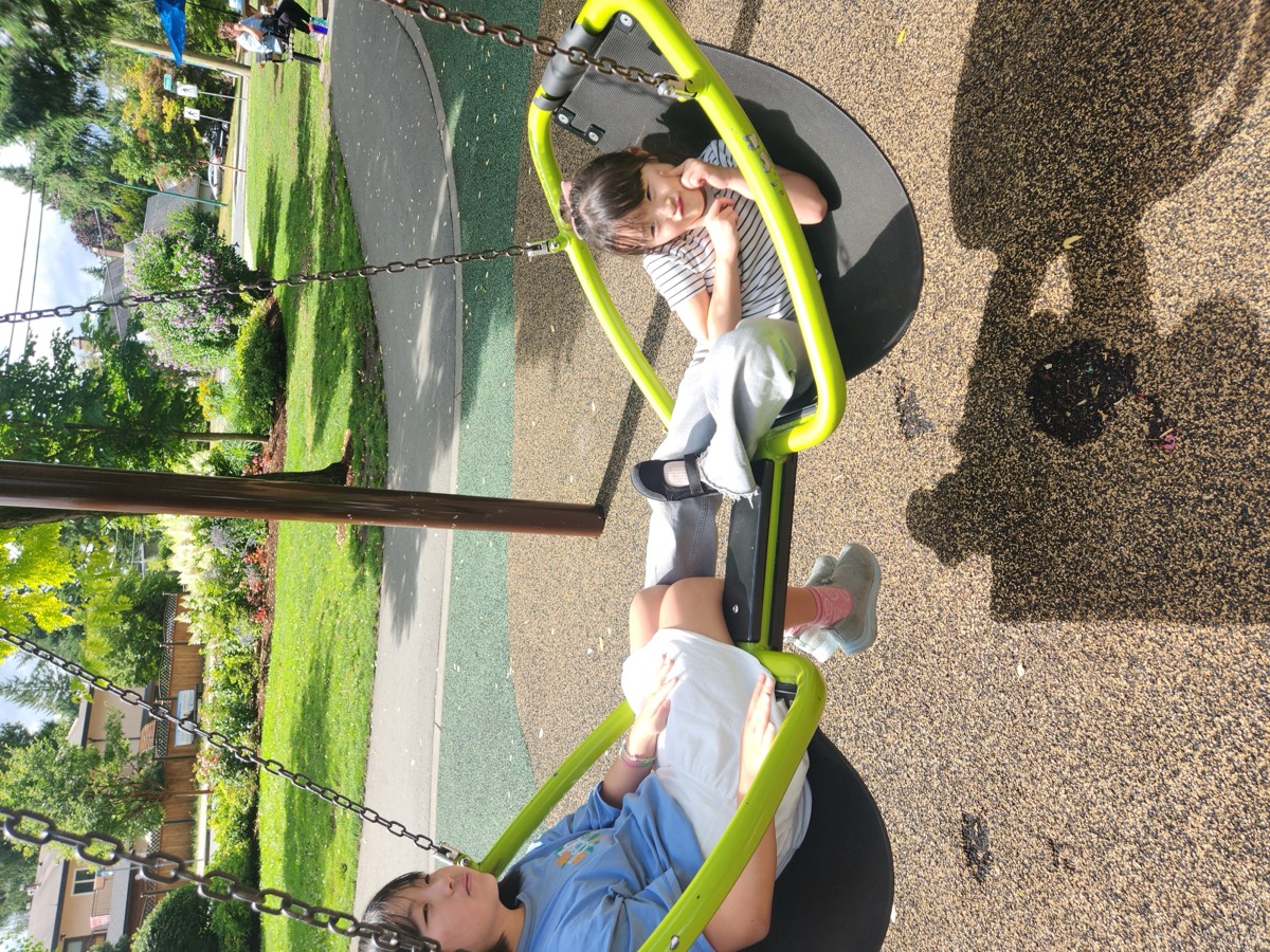 Two students lounging back on a green bucket swing at the playground