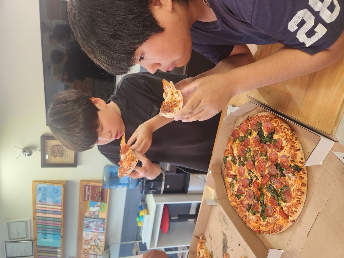 Two boys taking big bites of pepperoni pizza beside an open pizza box