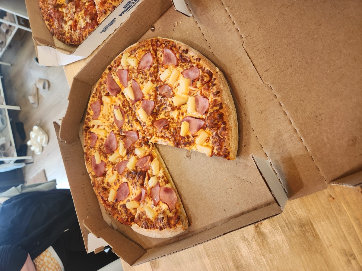 A close-up of a Hawaiian pizza with ham and pineapple in the box