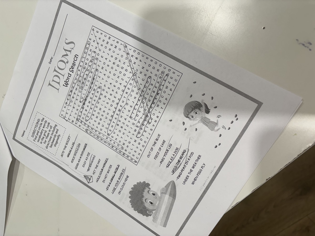 A completed idioms word search with words circled in pencil on the desk