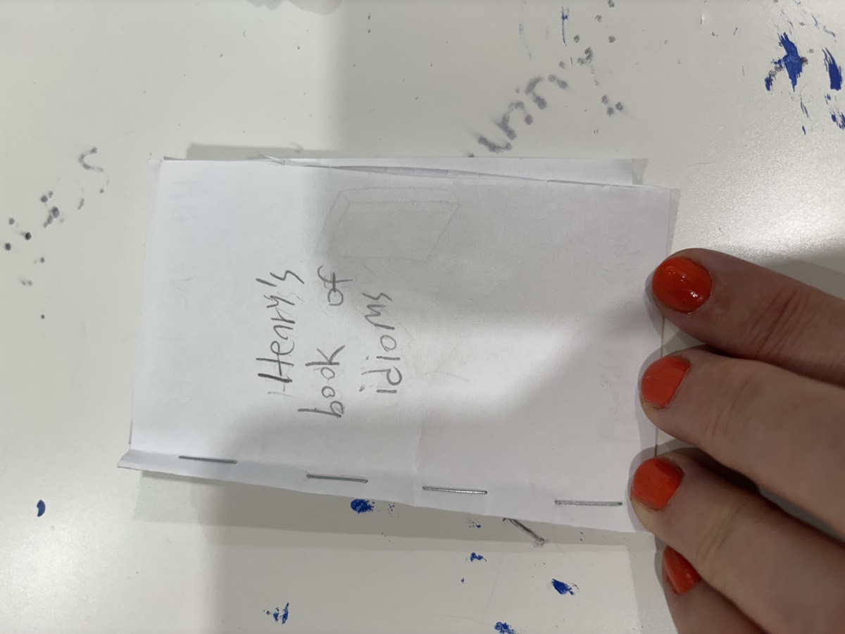 A handmade booklet cover reading Henry's book of idioms held up in a hand