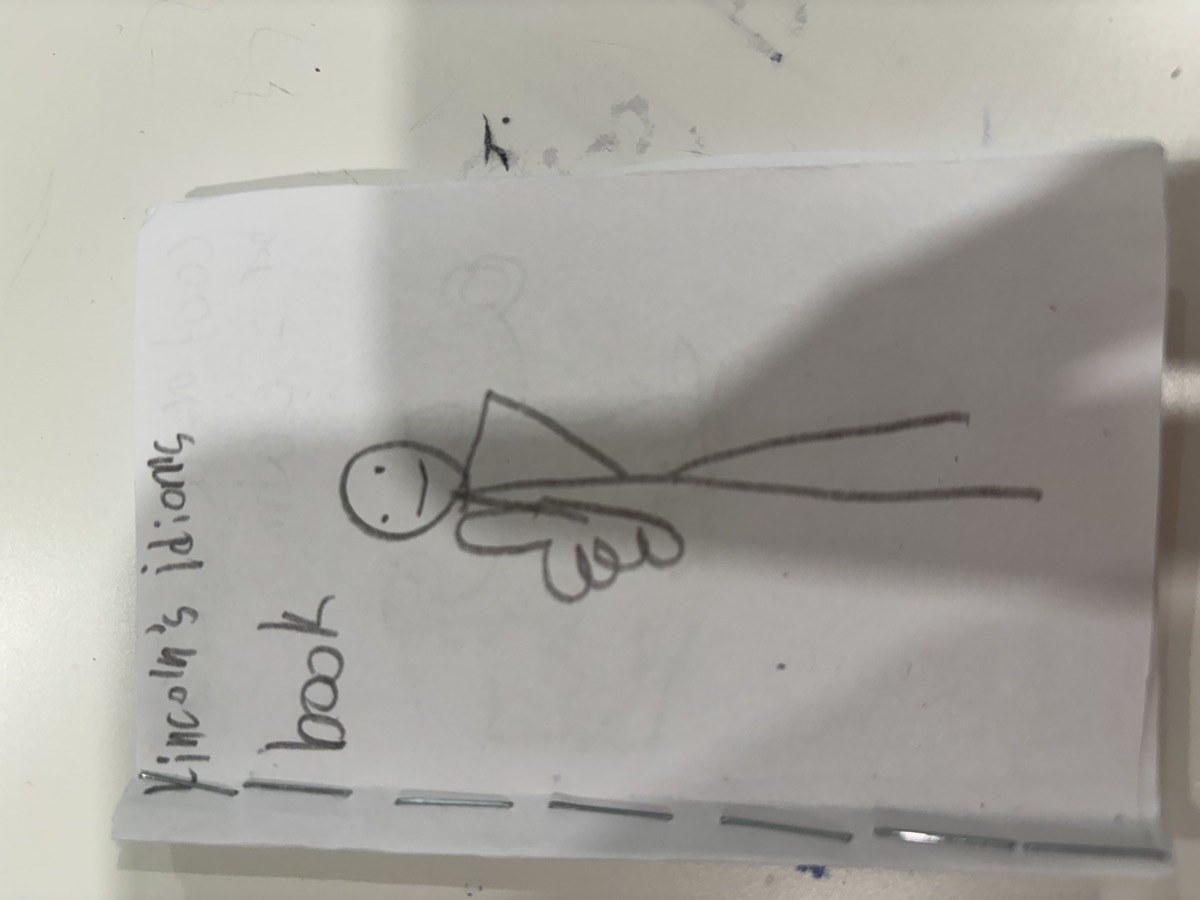 A handmade booklet cover reading Lincoln's idioms book with a pencil drawing of a stick figure giving a thumbs up