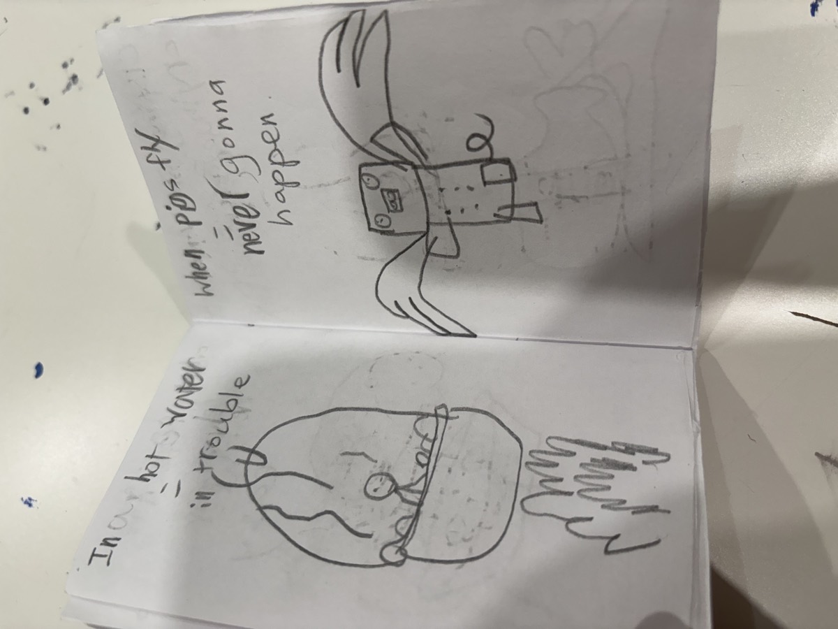 A pencil booklet spread reading In hot water equals in trouble and When pigs fly equals never gonna happen, with drawings of a figure in a pot and a flying pig