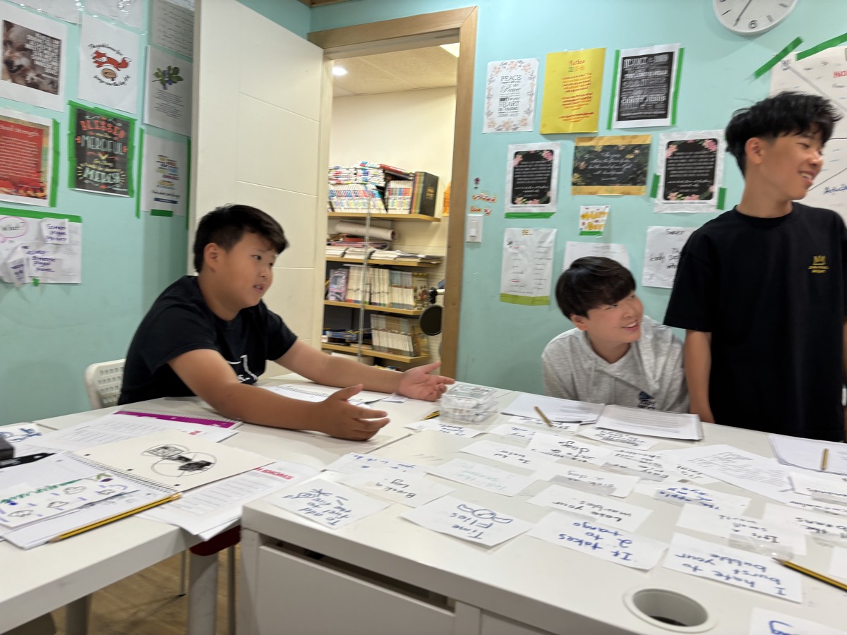 Students at the classroom table during Idiom Jeopardy, smiling as they answer