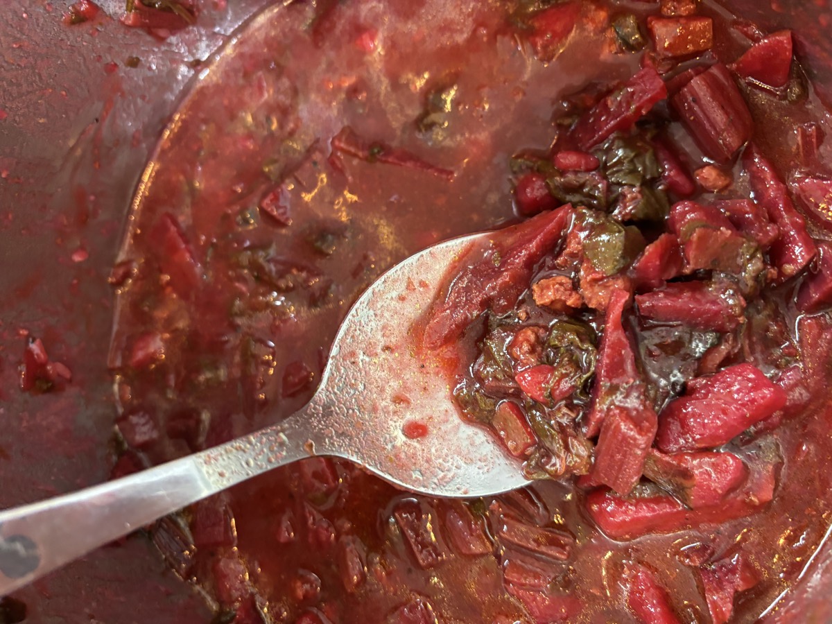 A large pot of deep red beef and beet borscht with a serving spoon in it