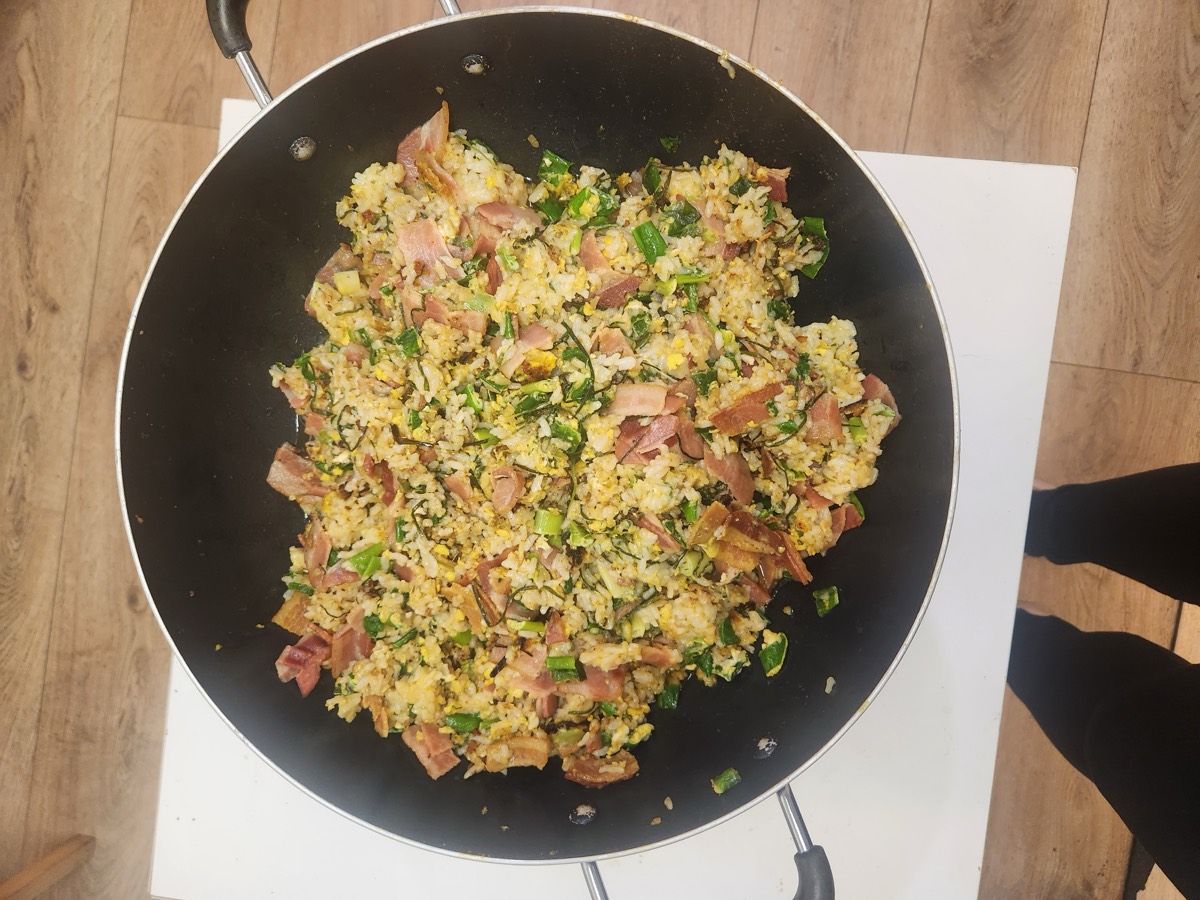 A wide pan of fried rice with ham, egg and green onion