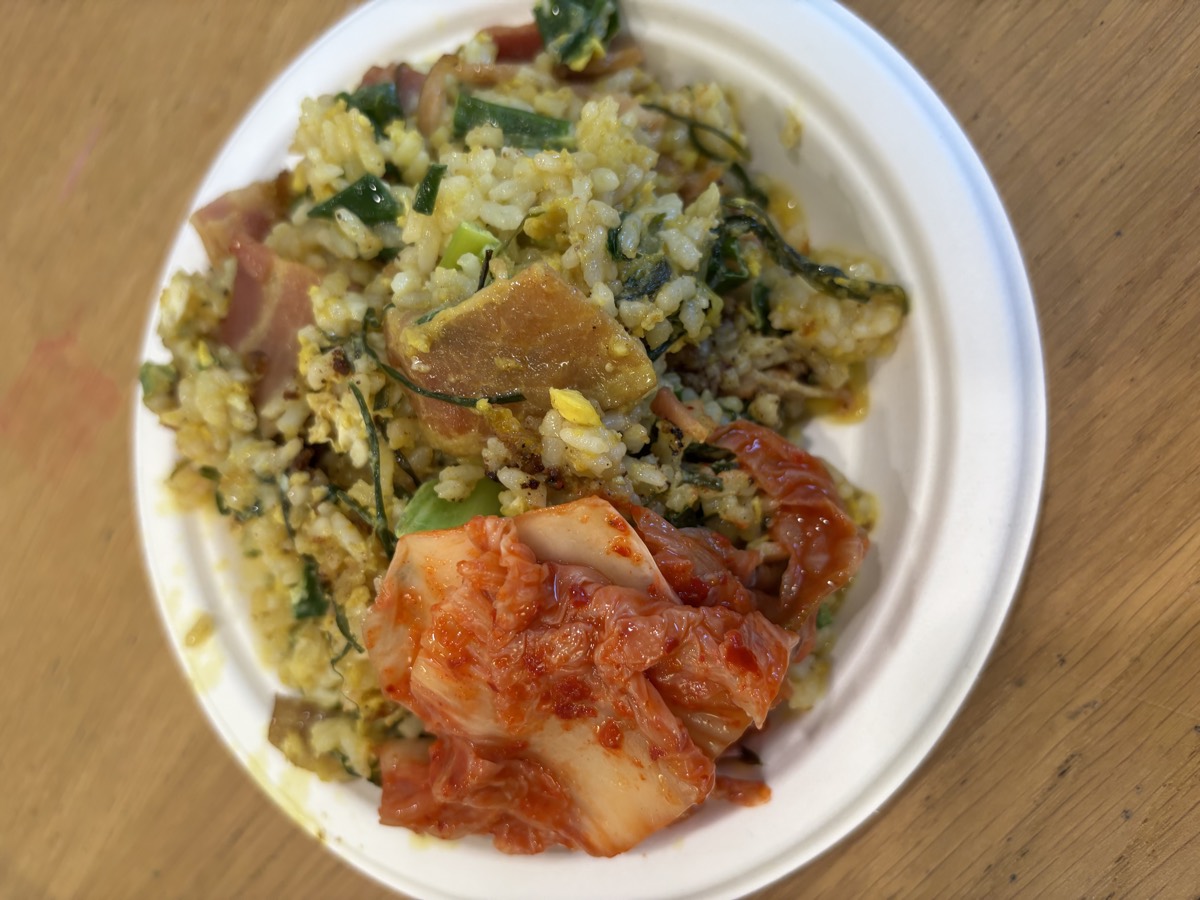 A paper plate with fried rice and a serving of kimchi on a wooden table