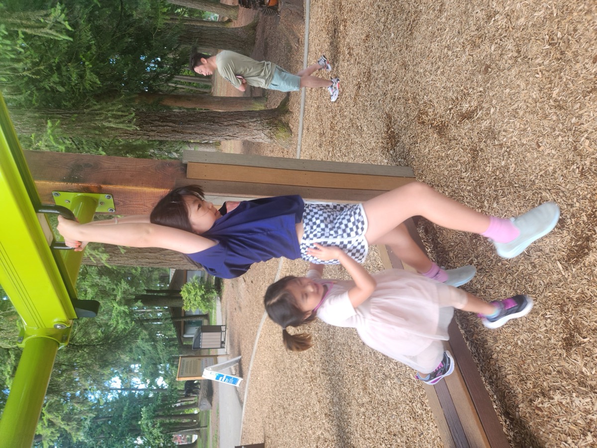 An older student hanging from a bar while a younger student climbs up beside her to try it too