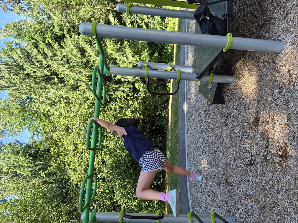 A student swinging hand over hand along the green monkey bars at the playground