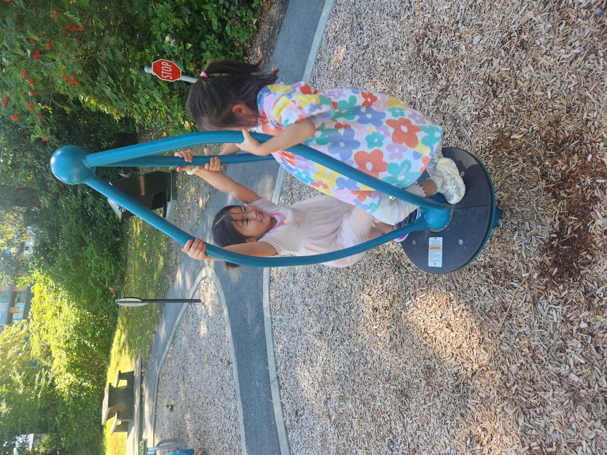 Two young students in dresses riding the standing spinner at the playground