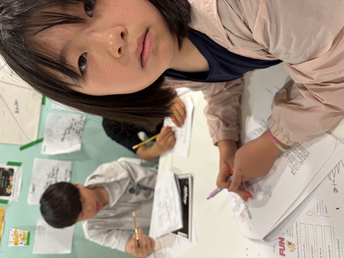 A student writing carefully in her booklet while a classmate works behind her