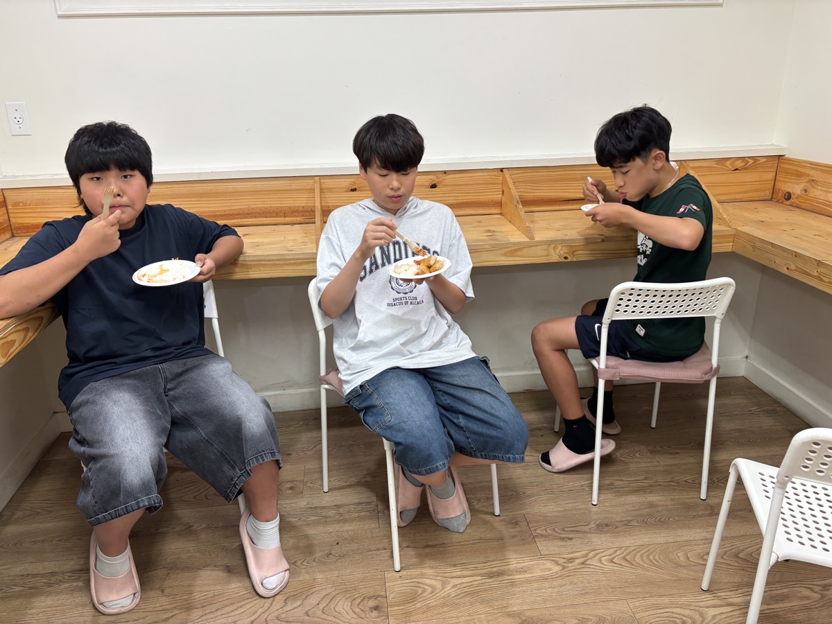 Three middle school students sitting in a row along the wall bench, eating lunch from their plates
