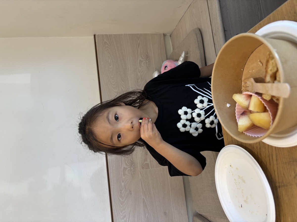 A young student eating fruit from a bowl at the table, plate cleared beside her