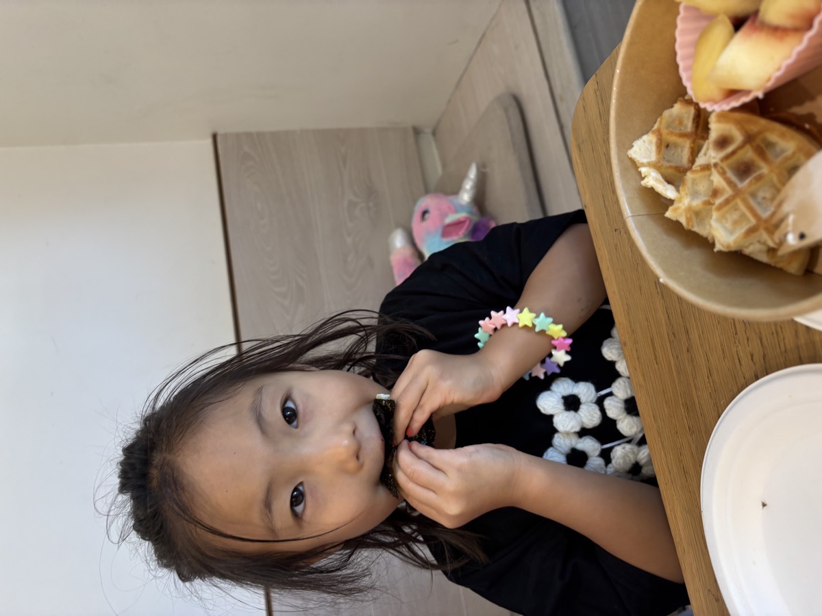 A young student taking a bite of a piece of roasted seaweed at the table