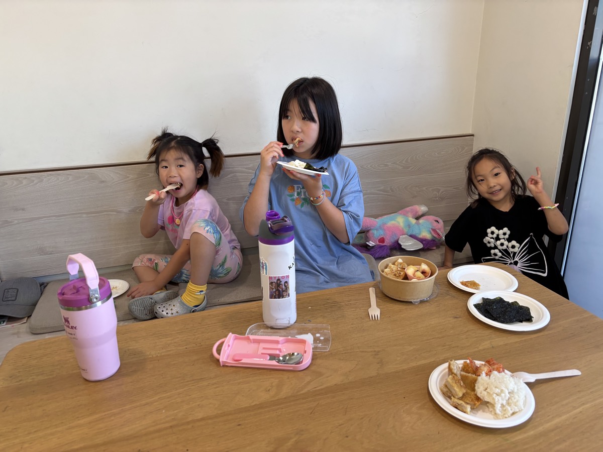 Three younger students sitting together at the lunch table, one making a peace sign at the camera