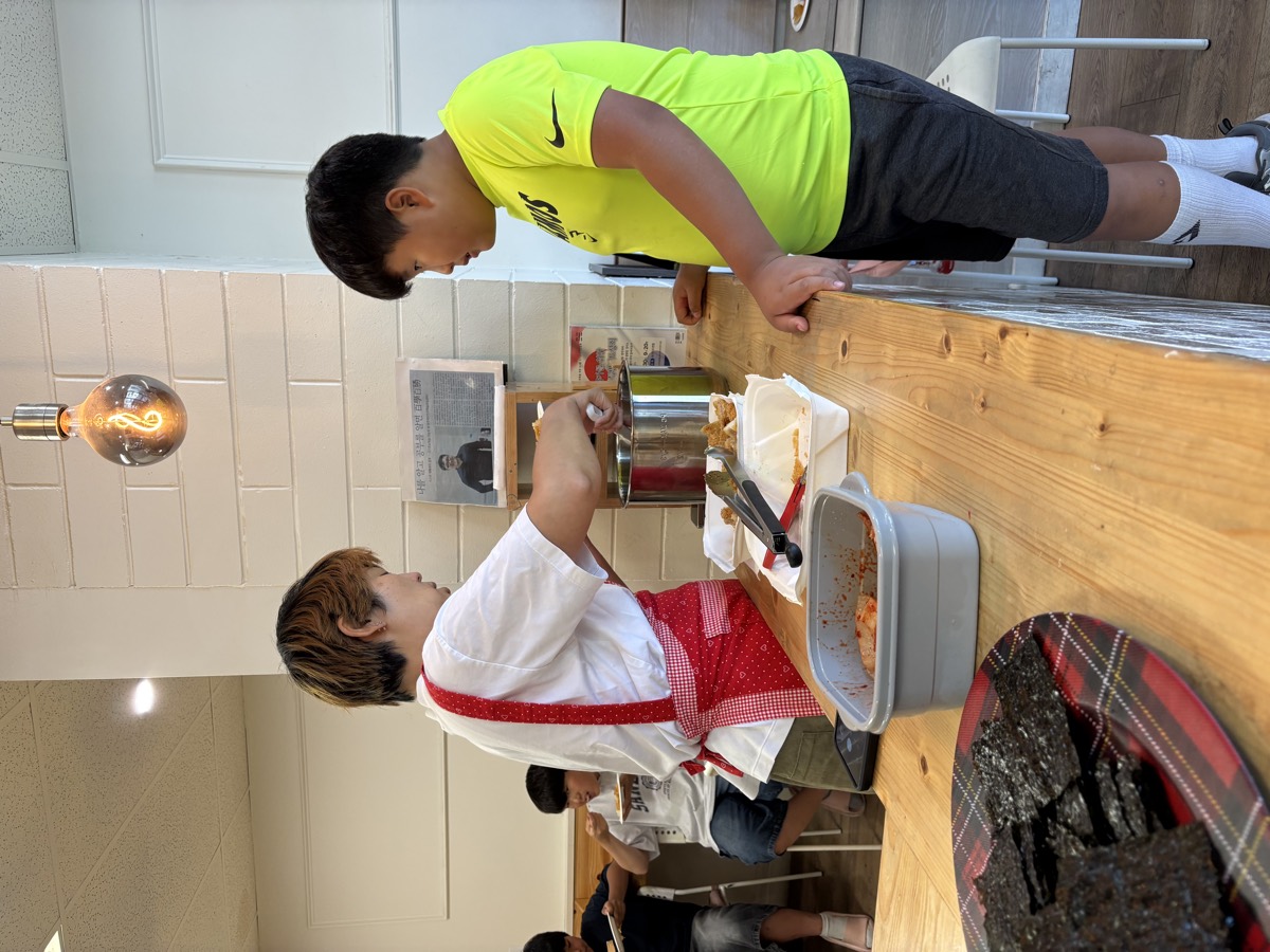 A teacher serving lunch at the counter while a student waits beside her with a plate