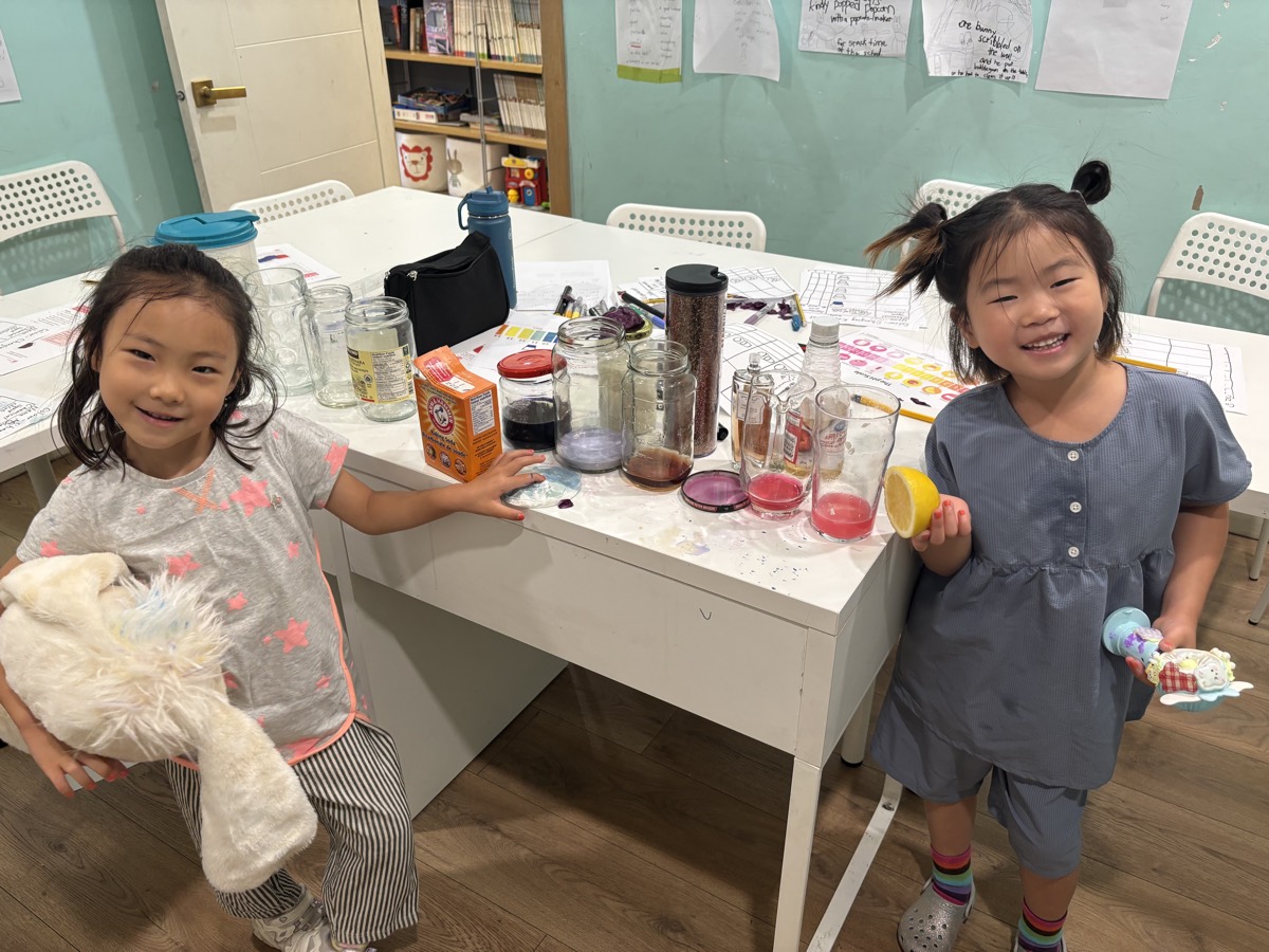 Two young students standing at either end of the table full of jars, both smiling at the camera