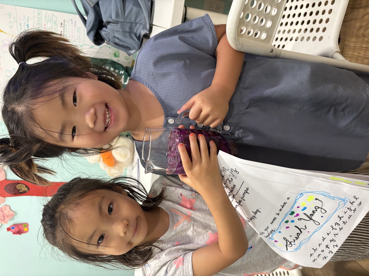 Two young students holding a jar of purple cabbage water together and smiling at the camera