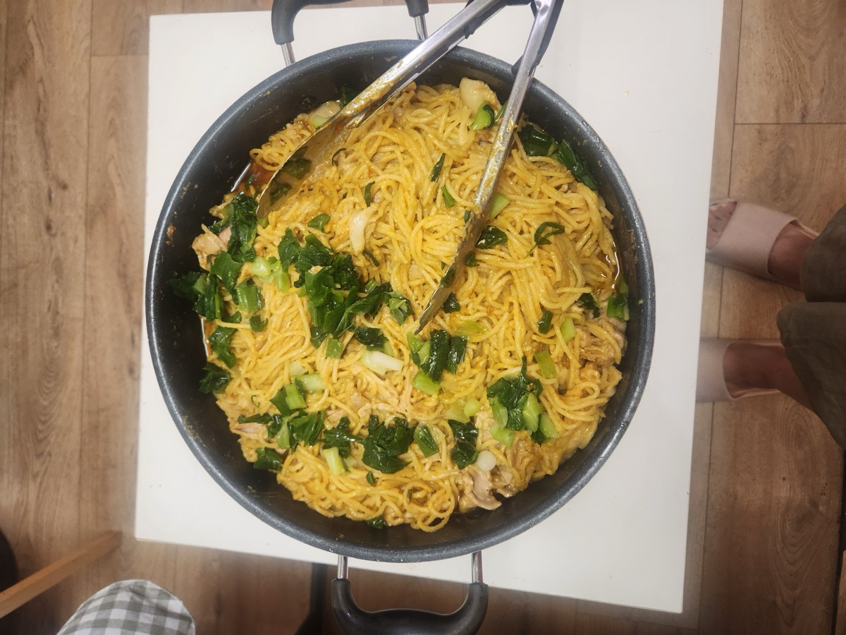 A large pan of noodles with vegetables and tongs resting in it