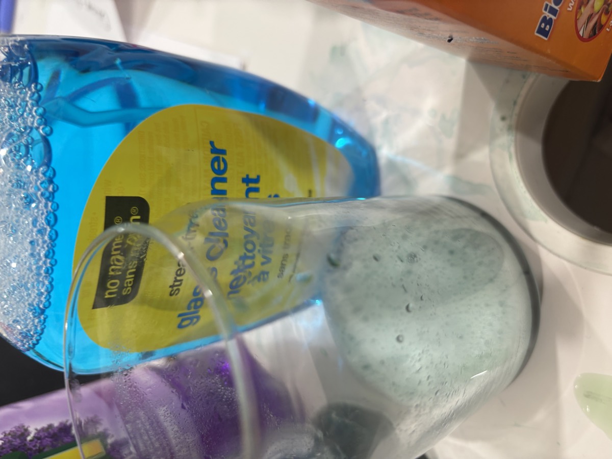 A jar of liquid turned bright blue beside a bottle of glass cleaner