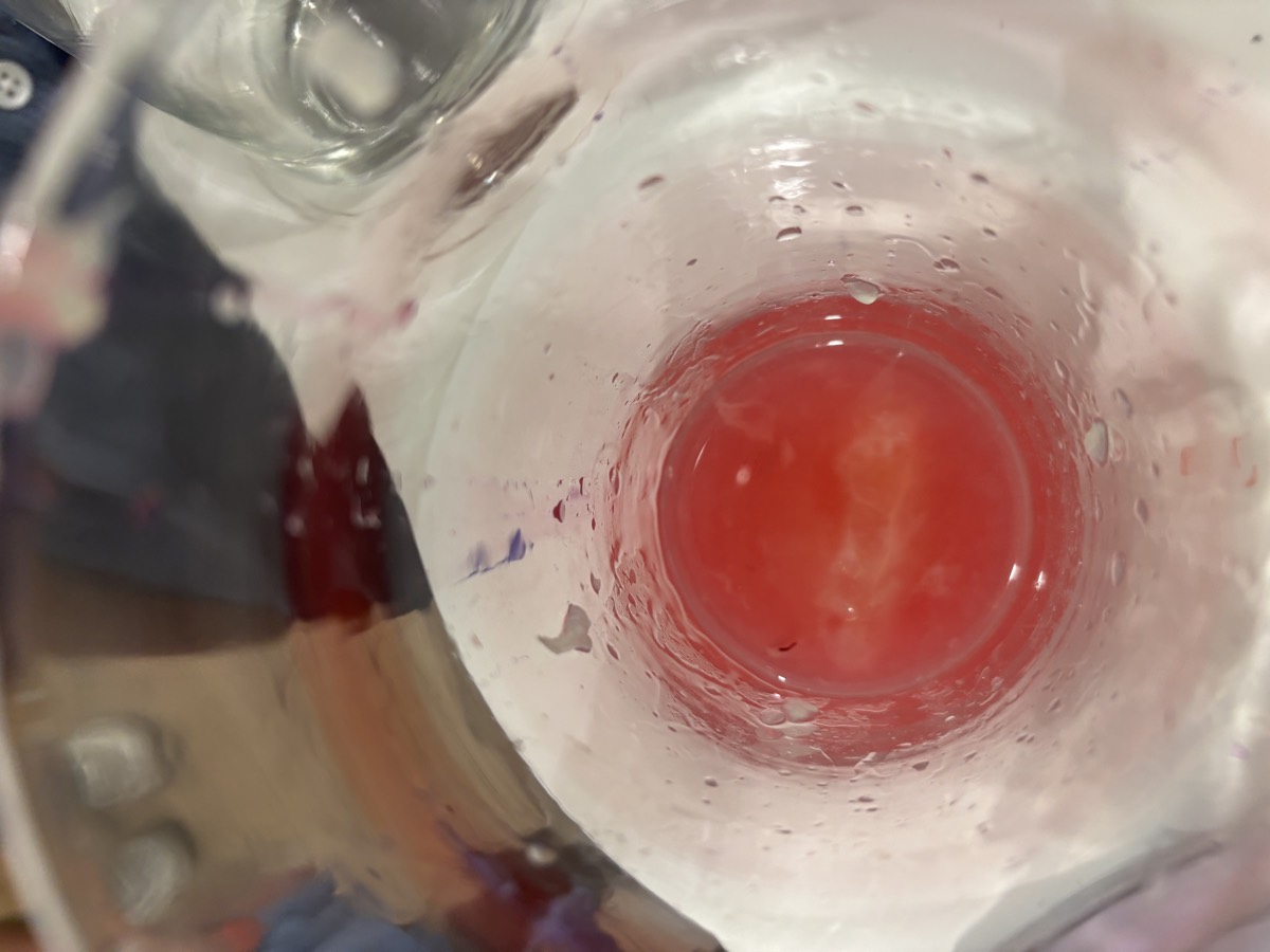 A close-up looking down into a glass where lemon juice mixed with cabbage water has turned a vivid bright red