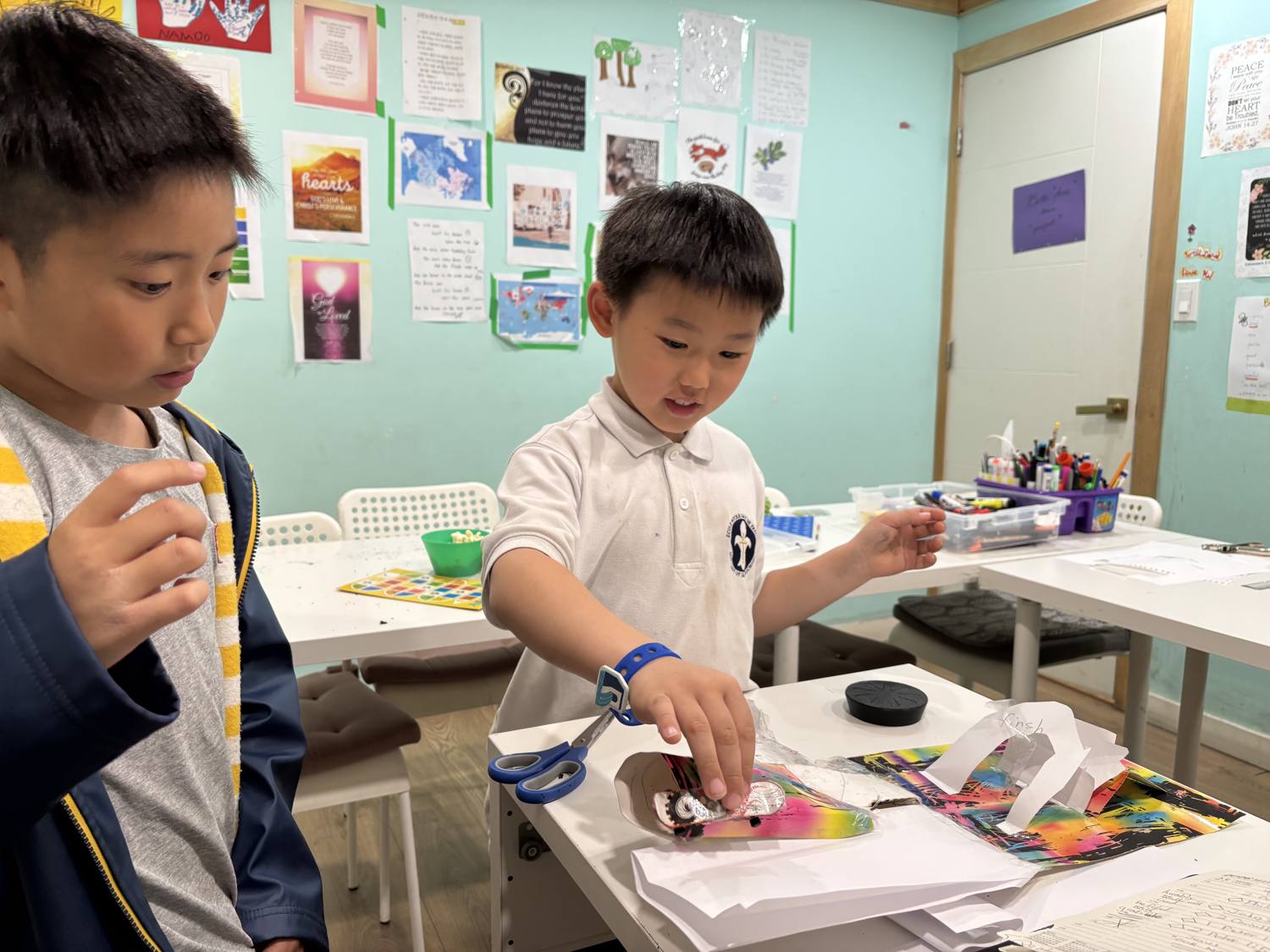 Two students cutting and assembling colourful paper art at the work table