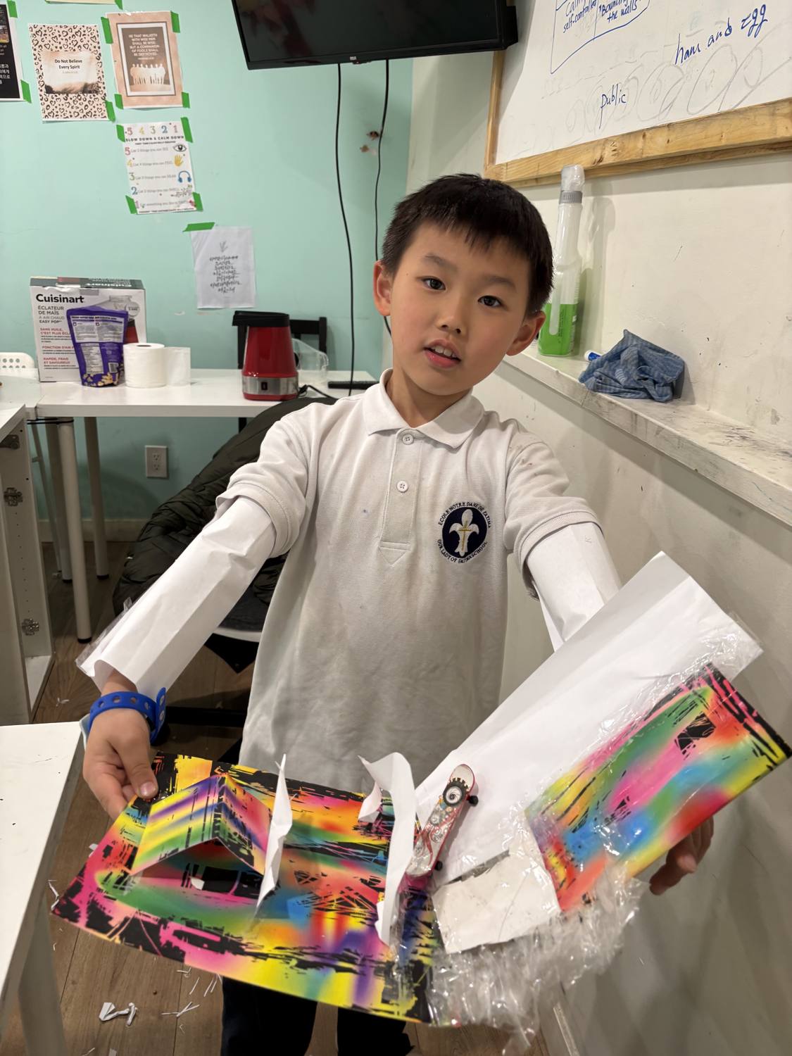 A proud student holding up his finished rainbow spray-paint art creation
