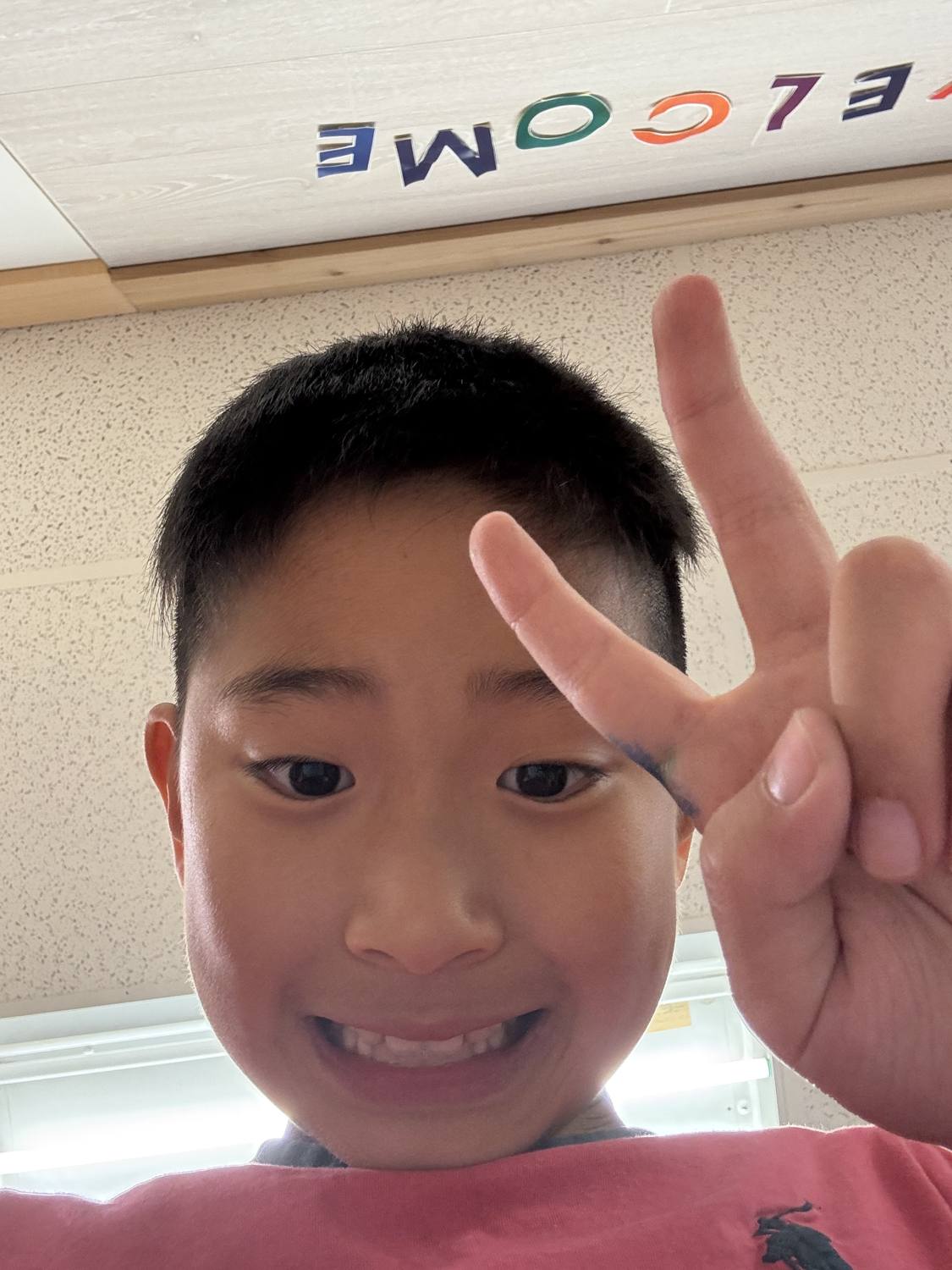 A happy student smiling and giving a peace sign by the WELCOME wall