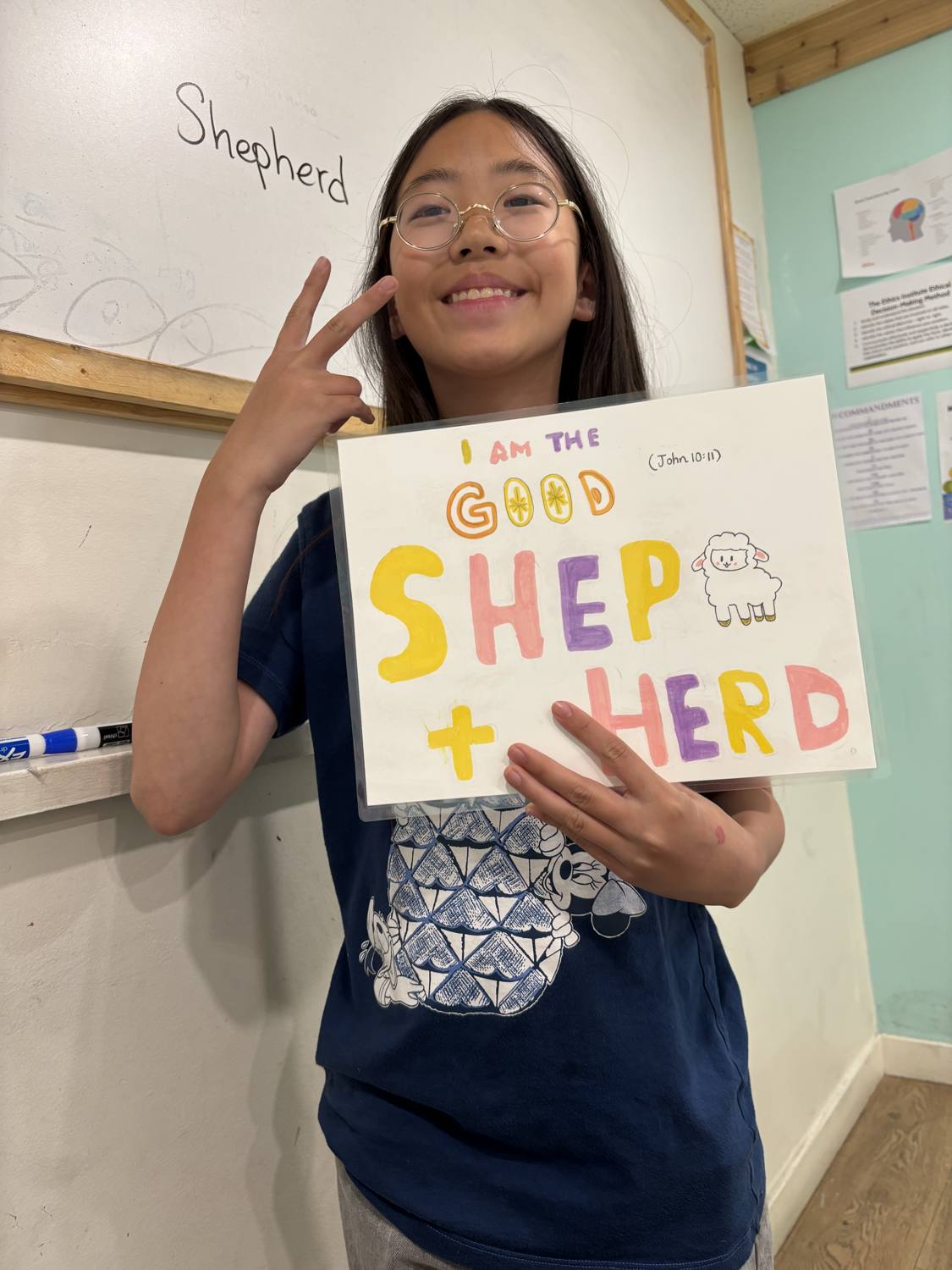 Yooha smiling and holding her hand-drawn 'I Am the Good Shepherd' artwork (John 10:11)